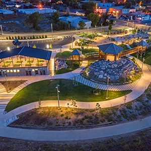 Aerial view of a well-lit park and community center at night, featuring winding pathways, green spaces, and a modern building structure in an urban area.